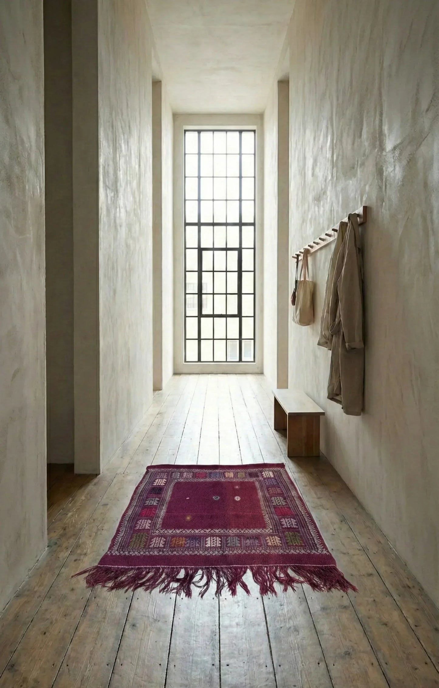 hallway with a red patterned Anatolian rug on wooden floor, wall hooks with coats, and large window.