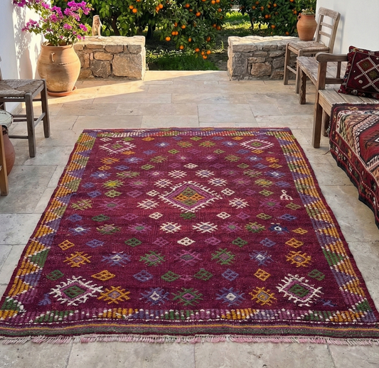 Colorful patterned rug on a stone patio with outdoor furniture and orange trees in the background.