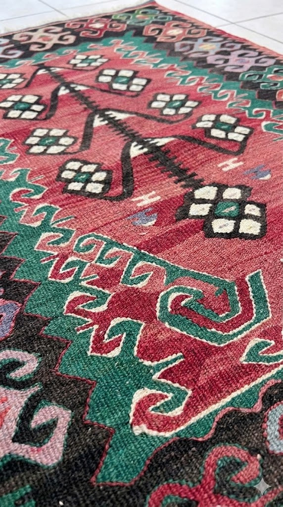 Traditional Turkish Kilim with a red field, central black-and-green geometric tree motif, and a multi-colored serrated border