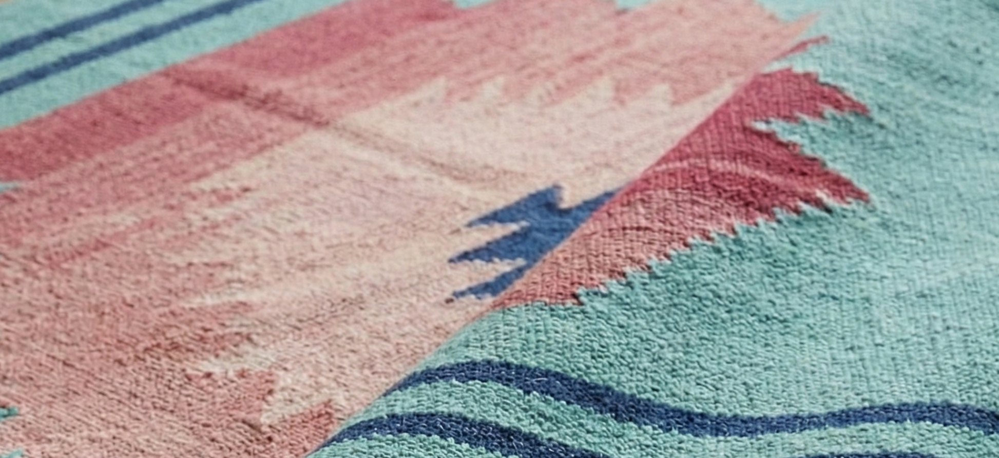 Close-up of a flatwoven Anatolian kilim rug with pink and blue patterns on a wooden floor