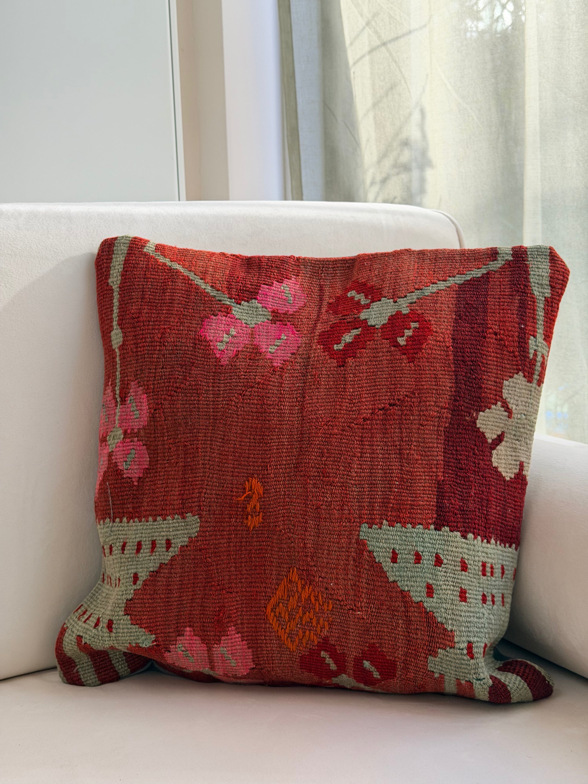 Handwoven rust-toned kilim cushion cover with delicate abstract floral patterns in sage green and dusty pink.