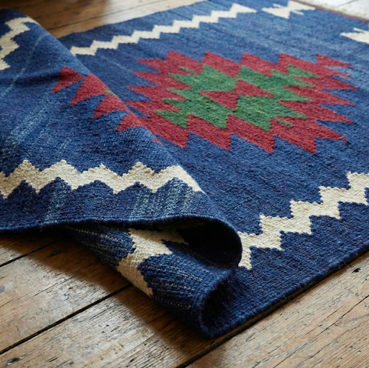 Blue patterned Anatolian kilim rug with red and green center on a wooden floor