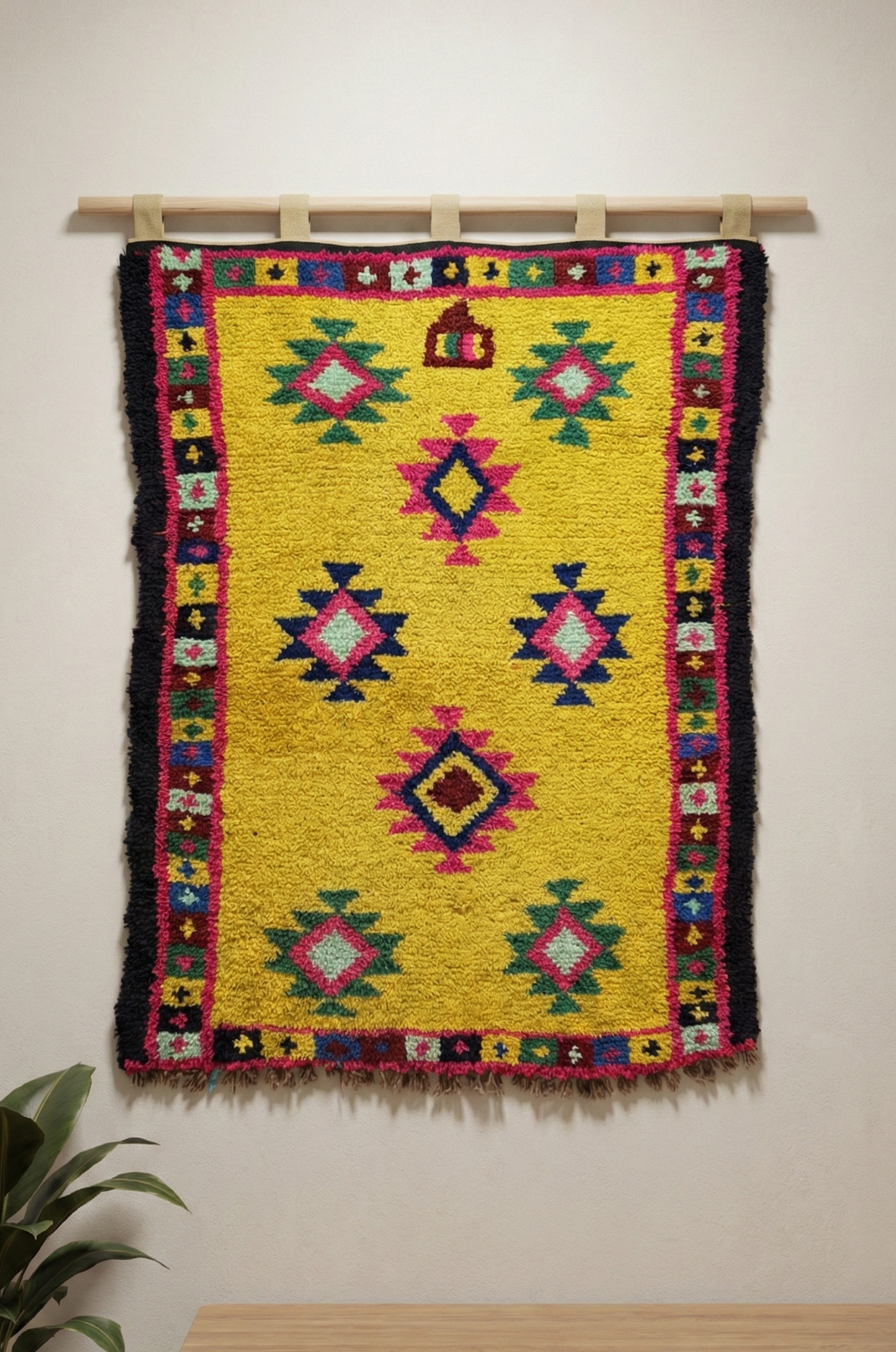 Colorful Anatolian wool rug hanging on a wall with a plant and table in the foreground