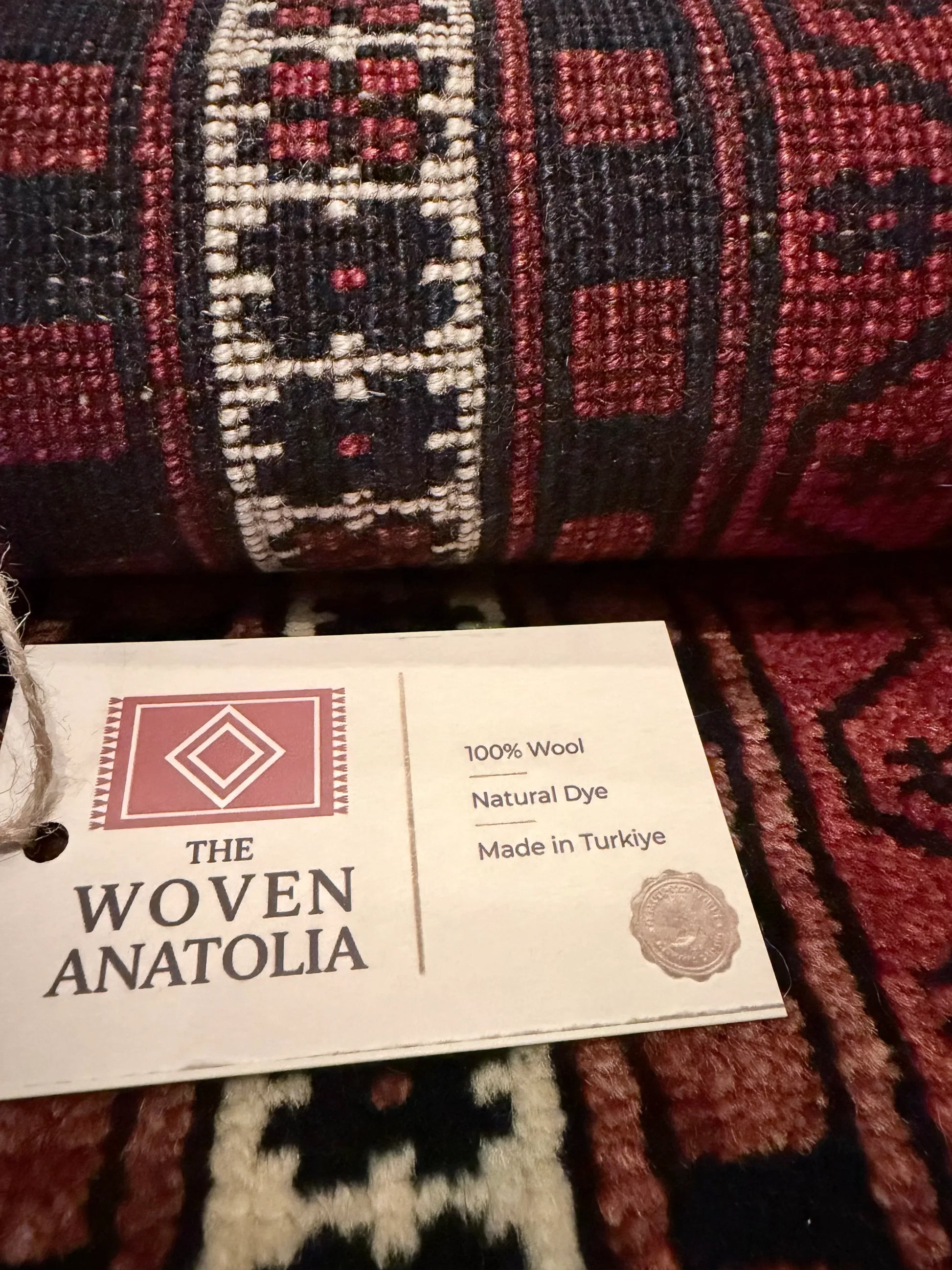 Close-up of a woven Anatolia rug with a label indicating it is made from 100% wool and natural dye